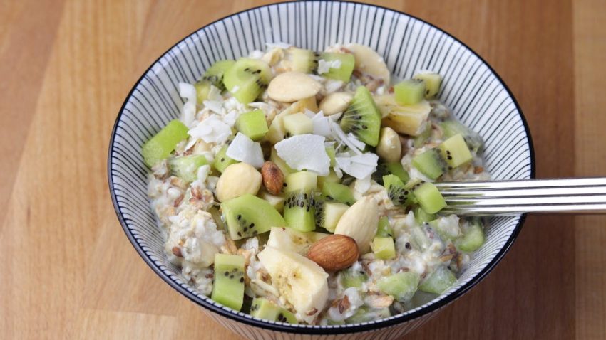 Vegan oat porridge topped with fresh fruits and nuts, served in a stylish ceramic bowl on a wooden surface.